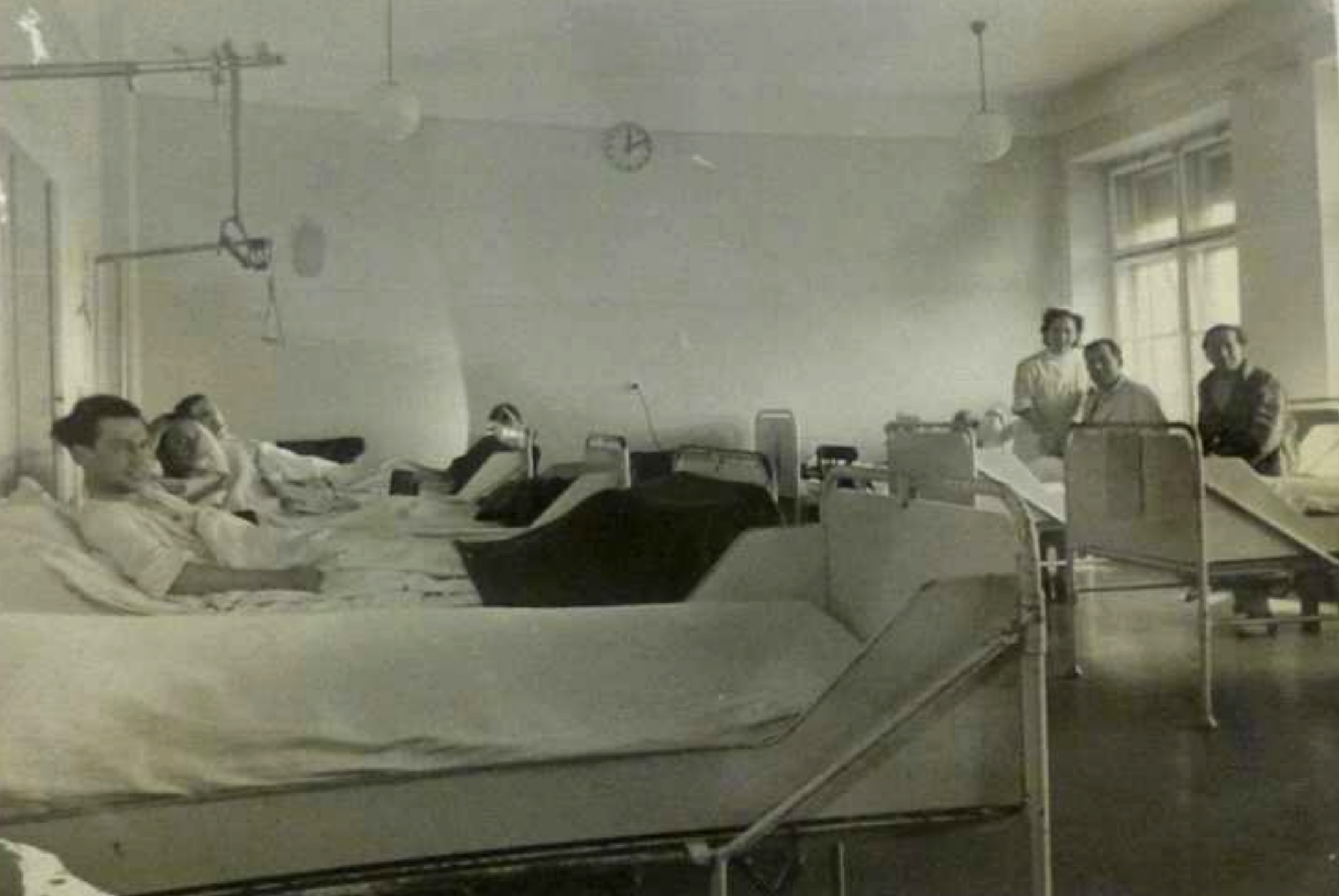 Schwarz-Weiß-Foto: Krankensaal mit fünf Patienten und einer Krankenschwester