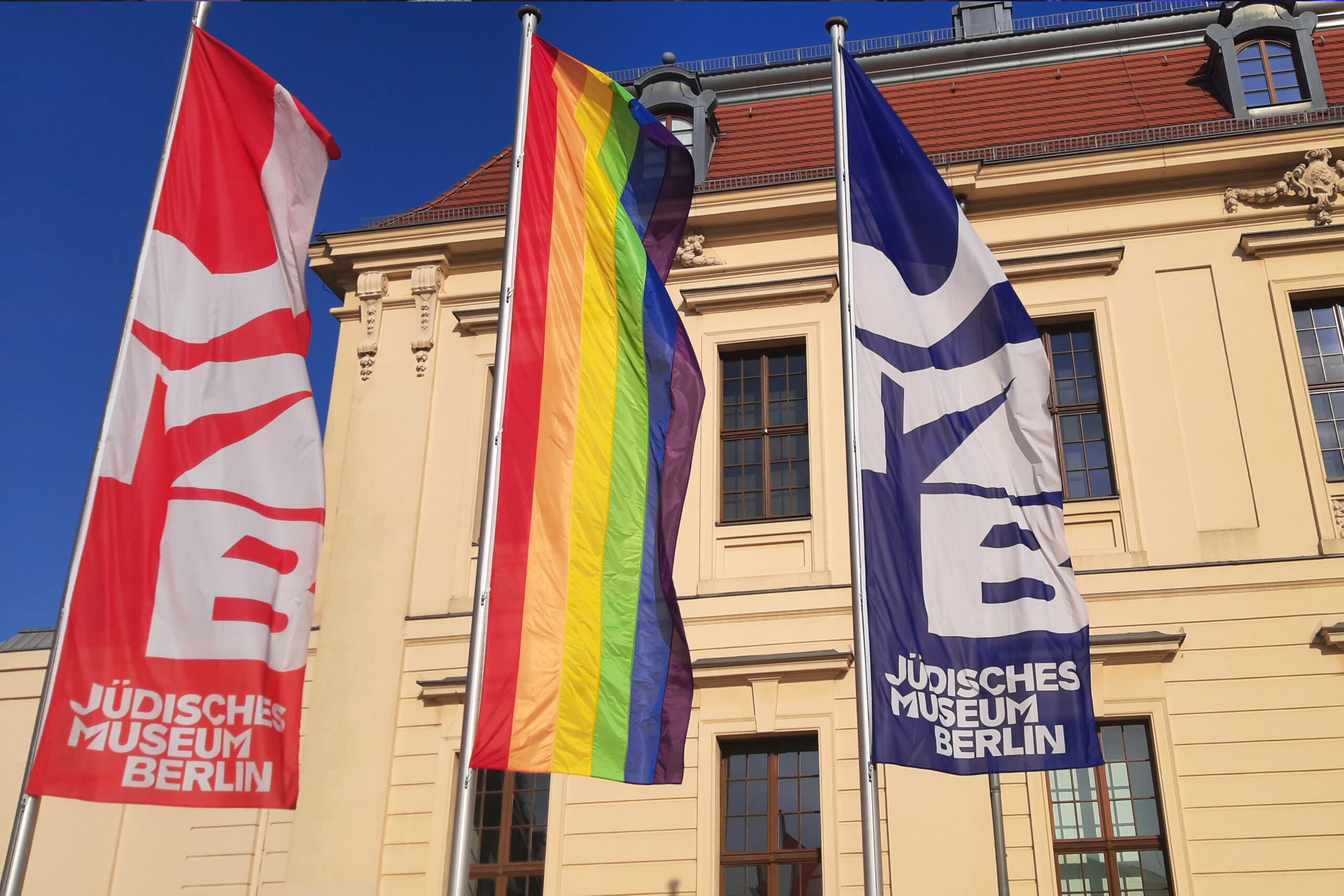 Eingang des Jüdischen Museums Berlin mit Flaggen des Museums und einer Regenbogenflagge