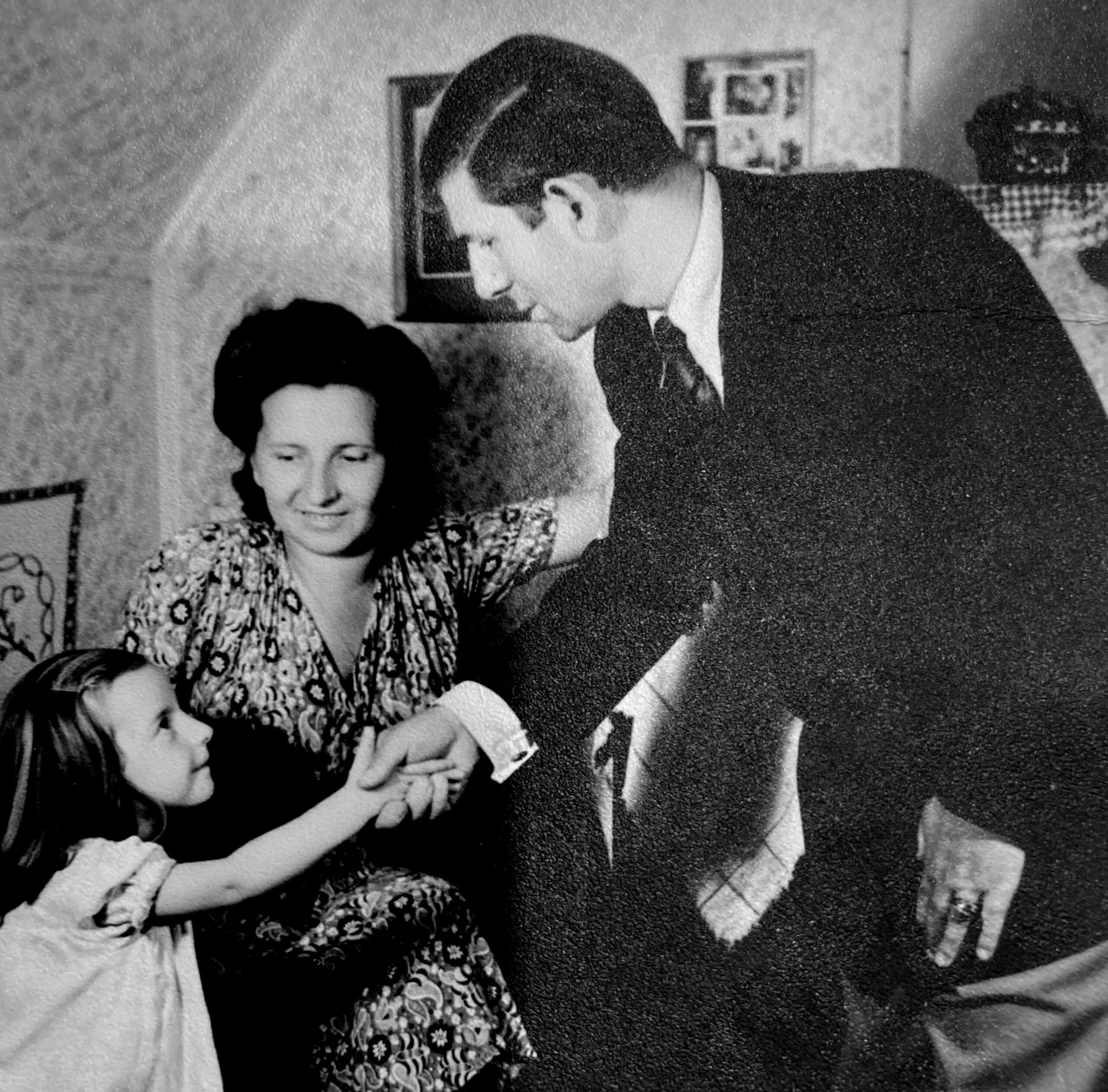 Familienfoto, Schwarz-Weiß: Vater, Mutter und ein kleines Mädchen, alle festlich gekleidet. Der Vater schüttelt dem Mädchen die Hand.