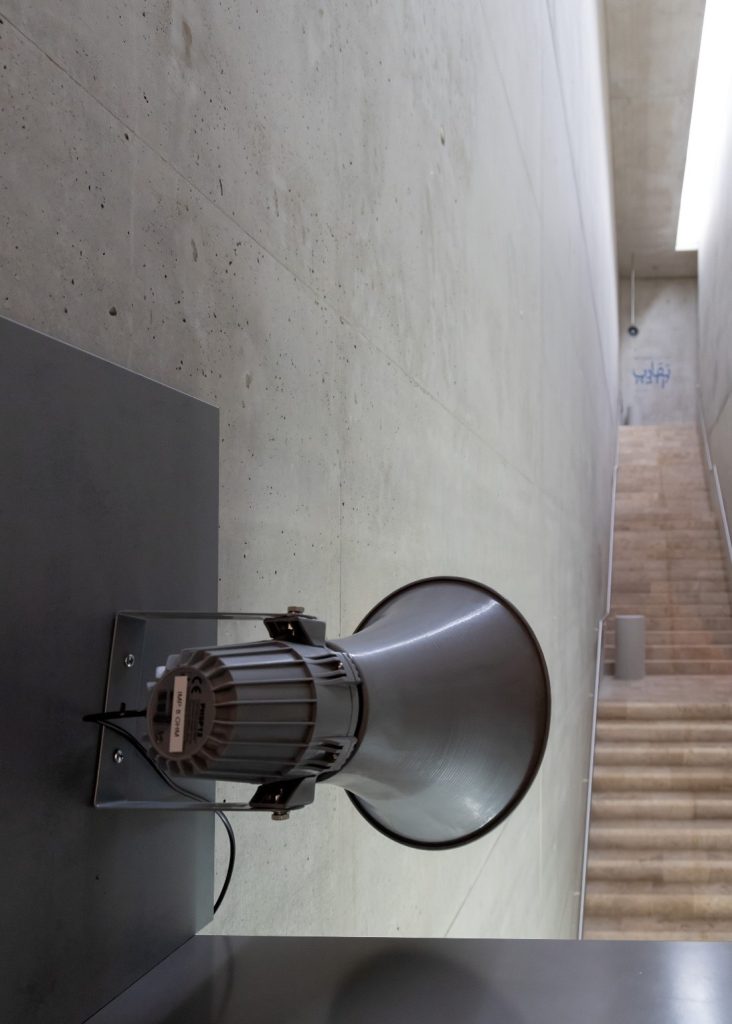 Auf dem Foto ist das Treppenhaus des Jüdischen Museums zu sehen. Vorne im Bild ist ein Lautsprecher in Richtung der Treppe angebracht.