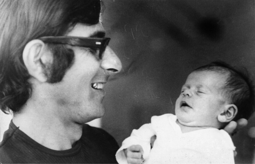 Andrei Spitzer holds his sleeping baby Anouk in his arms and smiles at her.