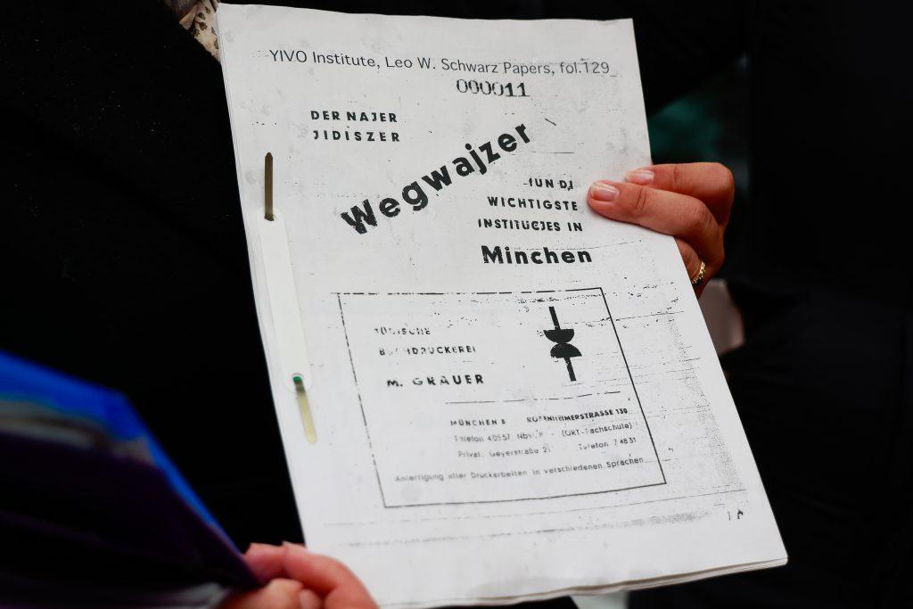 Sapir hält ein ausgedrucktes Heft in die Kamera mit einer Kopie des jiddischsprachigen Wegweisers.