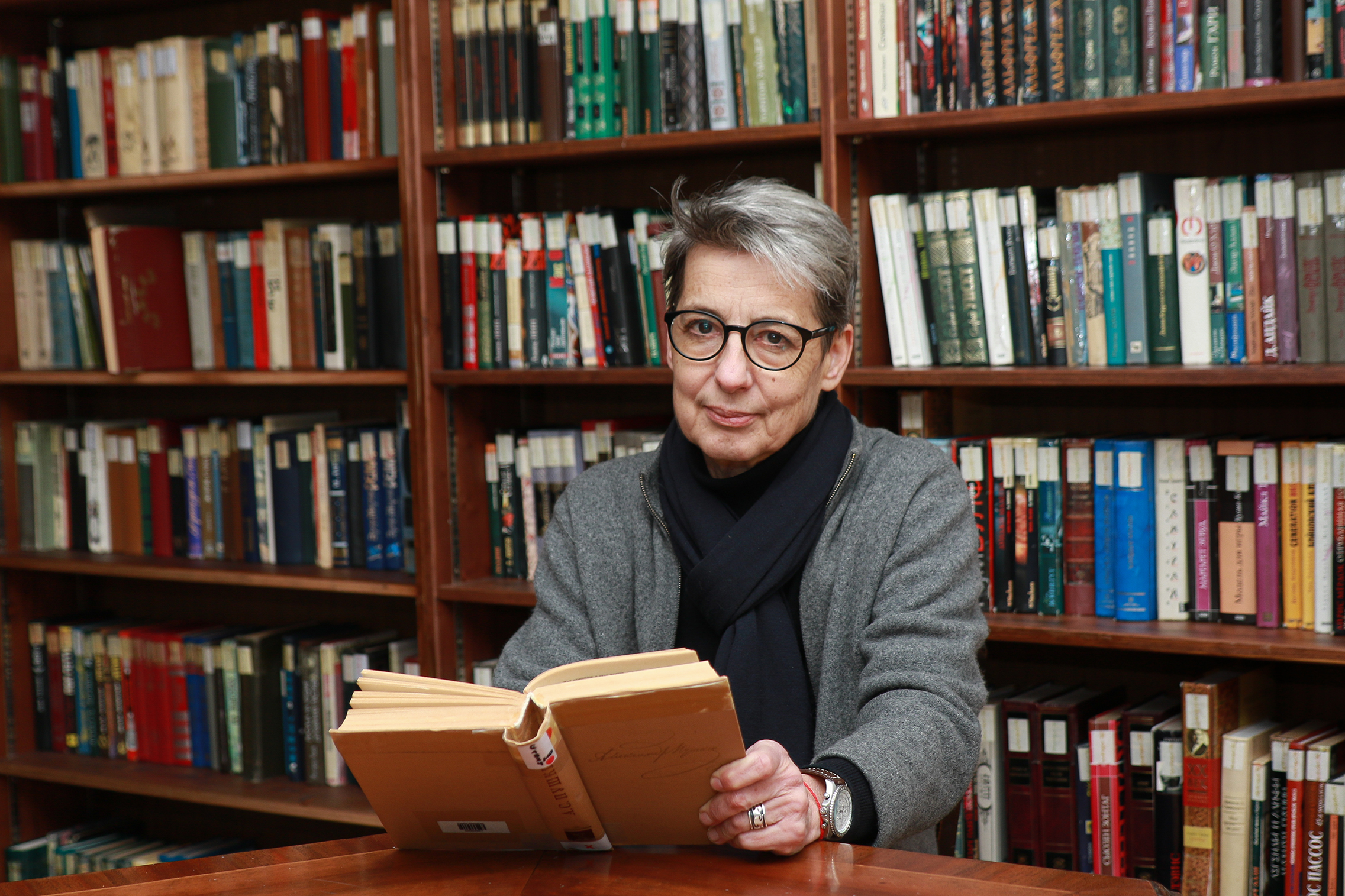 Tatjana Erschow sitzt an einem Tisch vor einer Bücherwand. Vor ihr liegt ein aufgeschlagenes Buch.