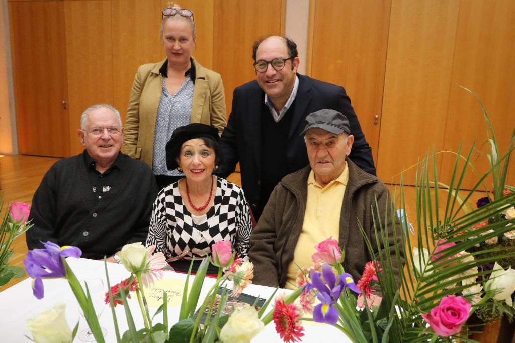 Gruppenfoto von 5 Personen an einem Tisch mit Blumen.